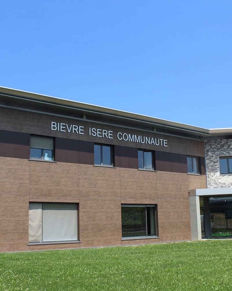 The brick and glass frontage of the Bièvre Isère Communauté offices, its name lettered across the upper storey above a strip of lawn