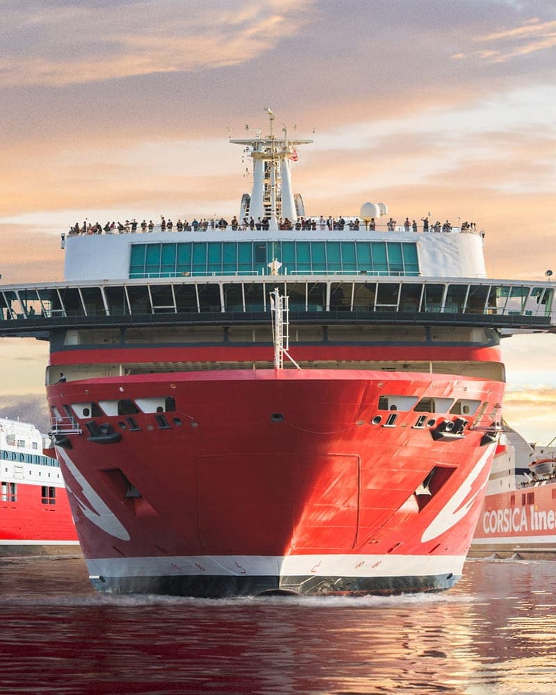 A red-hulled passenger ferry moored at sunset, travellers lining its upper decks